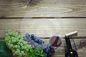 Open bottle of red wine with a glass, corkscrew and ripe grape on a wooden background. Copy space.