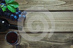 Open bottle of red wine with a glass, corkscrew and ripe grape on a wooden board. Copy space and top view.