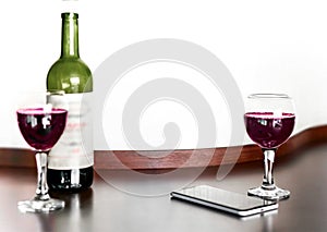 Open bottle and two glasses of red grape wine and mobile phone on brown wooden table and white blurred wall background. Alcohol dr