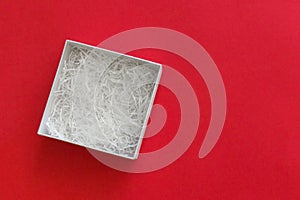Open box with filling material inside lying on a left side of red colored paper background, top view with copy space