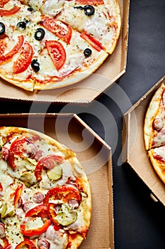 Open boxes with hot tasty italian sliced three pizzas on black background, delicious fast food, delivery concept, top view, copy s