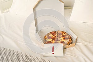 Open box of pizza on the big bed and card with Exclamation point. Concept