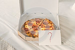 Open box of pizza on the big bed and card with question mark. Concept.