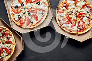 Open boxes with hot tasty italian sliced pizzas on black background