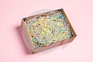 Open brown box with colorful pastel shredded paper on pink background