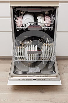 Open built-in dishwasher with clean dishes in white kitchen