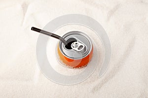 An open can of sweet carbonated drink with a drinking straw into a pile of granulated sugar. Top view, selective focus. Concept -