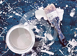 Open can of white paint with brush on blue wooden background