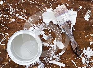 Open can of white paint with brush on wooden background