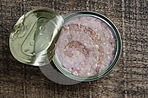 Open canned tuna in oil sauce on a wooden background, closeup, top view