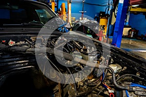 Open car hood without engine being repaired in a car mechanic`s garage. Showing wires and piping parts of a car`s engineering