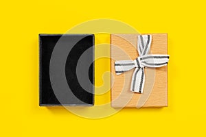 Open cardboard box with lid decorated with ribbon bow for gift packaging, yellow background, top view, copy space for
