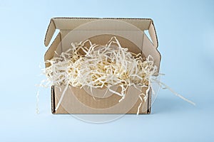 Open cardboard box package with shredded paper on blue background. Craft paper box for gift. Shipping eco package. Delivery pack,