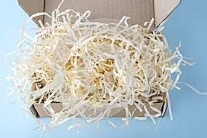 Open cardboard box package with shredded paper on blue background. Craft paper box for gift. Shipping eco package. Delivery pack,