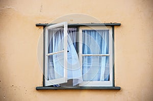 Open casement window in old stucco house with white gauze sheer curtains blowing out of them - close-up