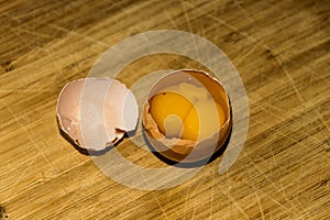 Open chicken egg with two yolks and its shell on wooden surface