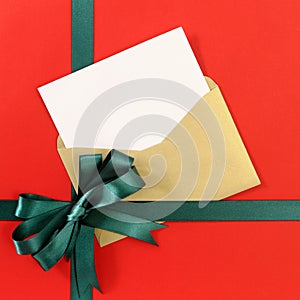 Open Christmas or birthday card with green gift ribbon bow on plain red background paper, copy space, vertical