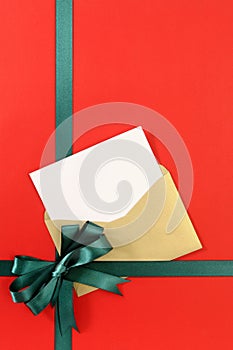 Open Christmas or birthday card with green gift ribbon bow on plain red wrapping paper background, vertical