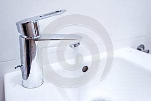 Open chrome faucet, tap washbasin in light room.