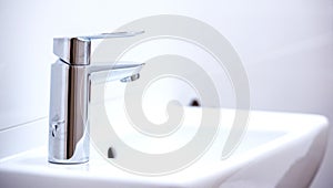 Open chrome faucet, tap washbasin in light room.