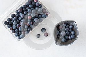 Open clamshell container of blueberries on a white granite counter, small black bowl