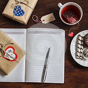 Open a clean blank Notepad, Valentines Day homemade gifts, a Cup of tea and sweets on wooden brown table.