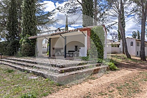 An open construction with a fireplace in a white country house with red wooden shutters on the balconies and gardens with many