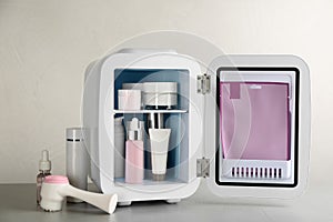 Open cosmetic refrigerator and skin care products on beige background