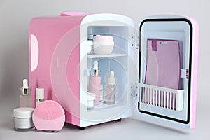 Open cosmetic refrigerator and skin care products on light background