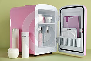 Open cosmetic refrigerator and skin care products on light green background