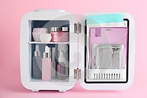 Open cosmetic refrigerator with skin care products on pink background