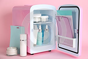 Open cosmetic refrigerator and skin care products on pink background