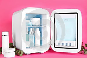 Open cosmetic refrigerator and skin care products on pink background