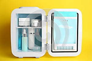 Open cosmetic refrigerator with skin care products on yellow background