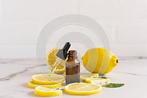 Open cosmetic vial with a dropper dropper filled with cosmetic lemon oil on a white marble background. lemon slices, melisa leaves