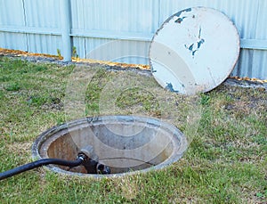 Open cover of concrete channel with main water valve of irrigation system and plastic hose. Concrete tube in ground