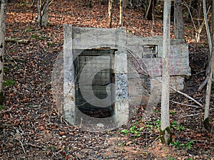 Open dark spooky entrance to the cold hidden catacomb in autumn forest with fallen brown leaves on the ground photo