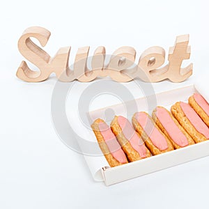 Open delivery paper box with six fresh pink cupcakes and wooden word Sweet on white background. Romantic gift. Unhealthy