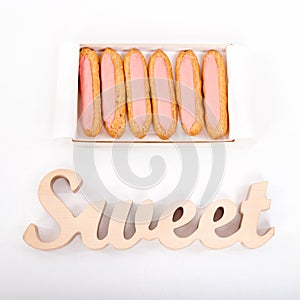 Open delivery paper box with six fresh pink cupcakes and wooden word Sweet on white background. Romantic gift. Unhealthy