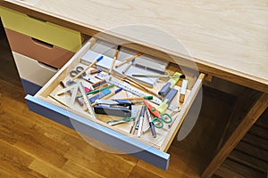 Open desk drawer with unsorted various school supplies