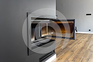 Open, dirty corner pane in a modern fireplace with a closed combustion chamber standing in the living room, painted black.