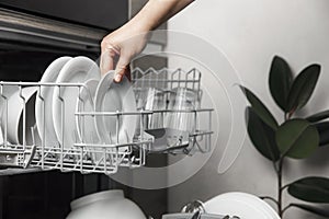 Open dishwasher with clean cutlery, glasses, dishes inside in the home kitchen