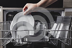 Open dishwasher with clean cutlery, glasses, dishes inside in the home kitchen