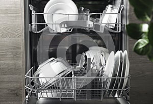 Open dishwasher with clean utensil inside, cutlery, glasses, dishes at kitchen