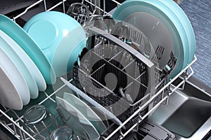 Open dishwasher with clean utensils in it,close up.Clean plates,glasses,forks,spoons after washing in the dishwasher.Dishwasher