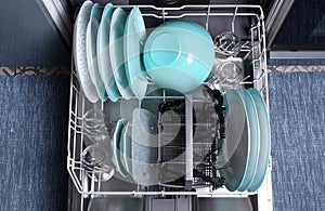 Open dishwasher with clean utensils in it.Top view.Clean plates,glasses,forks,spoons after washing in the dishwasher.Dishwasher