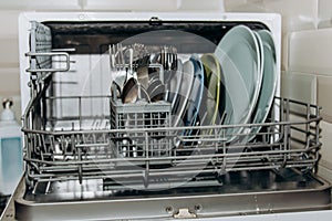 Open dishwasher close up clogged with clean washed dishes. dry cutlery closeup. spoons forks. mugs, plates. household appliances