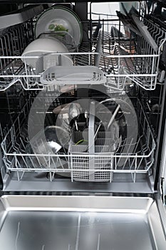 Open dishwasher with cutlery and plates as domestic appliance photo