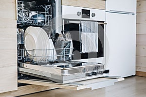 Open dishwasher with white clean dishes after washing in modern scandinavian kitchen