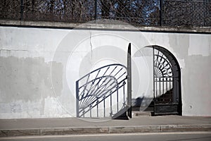 An open door of a wrought-iron gate in the wall. White cracked paint on the fence